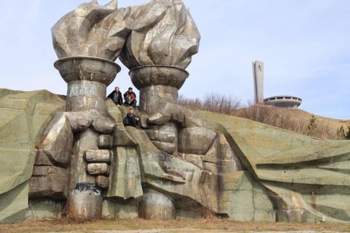 Travelers exploring socialist sculpture with torch-bearing hands at Buzludzha Monument Bulgaria