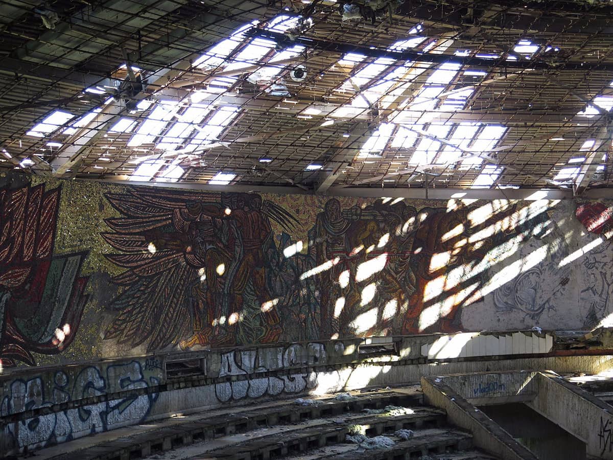 Interior of abandoned Buzludzha Monument showing damaged mosaic walls and broken ceiling with sunlight coming in