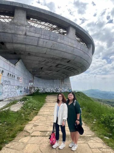 Tourists at side of Buzludzha Monument with panoramic mountain valley views in background