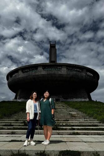 Two travelers on main staircase at Buzludzha Monument under dramatic stormy sky